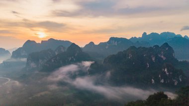 Güneşin doğuşuyla Khao Sok Ulusal Parkı Tayland 'ın nefes kesici manzarası engebeli dağların arasından süzülürken. Altın ışık huzurlu manzarayı aydınlatır.