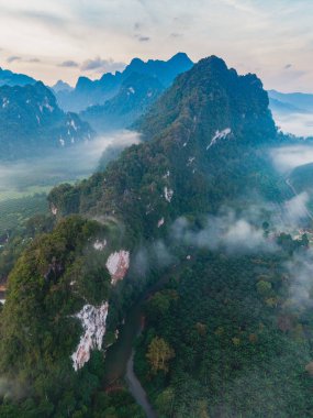 Sis, Tayland 'daki Khao Sok Ulusal Parkı' nın vadilerini sararken, dingin, yeşil tepeler görkemli bir gökyüzü altında yükseliyor. Bu tropik cennet macera arayanlar ve doğa severler için idealdir..