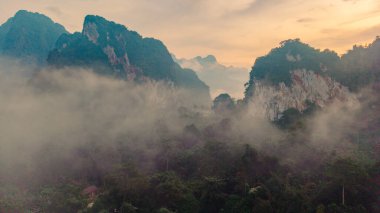 Güneş doğarken Tayland, Khao Sok 'un büyüleyici atmosferini tecrübe edin. Sis, yüksek dağları ve yemyeşil ormanları sarar. Keşif ve yansıtmayı davet eden sakin bir manzara yaratır..