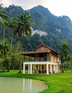 Huzurlu bir gölün yanında, Khao Sok Tayland 'daki bu güzel ahşap ev yüksek yeşil dağların büyüleyici manzarasını sunuyor..