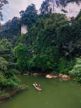 Tayland 'da Khao Sok nehrindeki bir bambu salında gezginler yüksek kireçtaşı kayalıkları ve yoğun ormanlarla çevrili. Bu resim gibi sahne, el değmemiş doğanın güzelliğini yakalar..