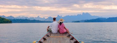 Çift, büyüleyici dağ manzarası ve yumuşak alacakaranlık renkleriyle çevrili Cheow Lan Gölü 'nde sakin bir tekne yolculuğunun keyfini çıkararak aşk ve macera için büyülü bir atmosfer yaratıyor. Khao Sok, Tayland