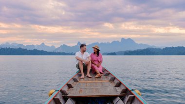 Kireçtaşı dağları ve renkli bir günbatımıyla çevrili Cheow Lan Gölü 'nde huzurlu bir akşamın tadını çıkaran bir çift. Doğa onları kucakladıkça sükunet hissedilir..