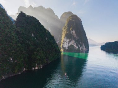 Sakin bir tekne, büyüleyici kireçtaşı kayalıkları ve canlı yeşilliklerle çevrili Cheow Lan Gölü 'nün el değmemiş sularında süzülüyor. Khao Sok, Tayland