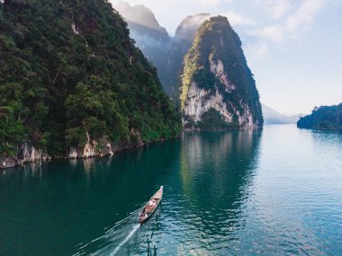 Uzun kuyruklu bir tekne, yüksek kireçtaşı kayalıkları ve canlı yeşilliklerle çevrili olan Cheow Lan Gölü 'nün sakin sularında süzülür. Huzurlu ortam Khao Sok Tayland 'ın doğal güzelliğini gözler önüne seriyor.