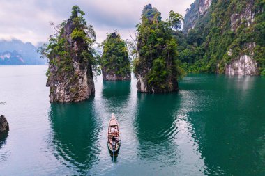 Kayık, etkileyici kireçtaşı kayalıkları ve yemyeşil yeşilliklerle çevrili Cheow Lan Gölü 'nün sakin sularında yavaşça süzülüyor. Tayland 'da huzurlu bir an doğal cennettir..