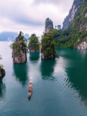 Yeşilliklerle bezenmiş kireçtaşı kayalıkları Cheow Lan Gölü 'nün turkuaz sularının üzerinde dimdik duruyor. Khao Sok Tayland
