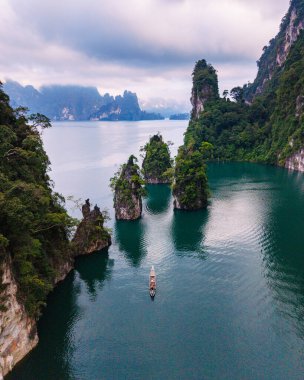 Yeşillik ve yüksek kireçtaşı kayalıklarıyla çevrili Cheow Lan Gölü 'nün sakin sularını keşfedin. Yalnız bir tekne huzurlu bir arazide süzülüyor, Khao Sok Tayland