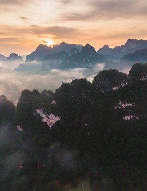 Büyüleyici güneşin doğuşuna tanık olun. Tayland, Khao Sok 'un yemyeşil dağlarına altın bir parıltı saçıyor. Sis yavaşça yükseliyor, büyüleyici ve huzurlu bir manzara yaratıyor, doğa severler için mükemmel..