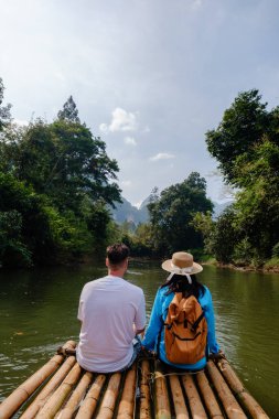 Bir çift, Tayland 'daki Khao Sok' un sakin suları ve yoğun ormanıyla çevrili bambu salında dinleniyor. Güneş parıldıyor, doğayı keşfetmek için huzurlu bir gün yaratıyor..