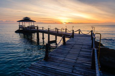 Tayland 'daki Koh Kood Adası' nın sakin sularında huzurlu bir gün batımı yaşayın. Ahşap iskele okyanusa doğru uzanıyor, akşam yürüyüşleri ve doğada rahatlama için mükemmel..