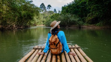 Bir gezgin bambu salında otururken Khao Sok Ulusal Parkı 'nın huzurlu atmosferinin tadını çıkarır. Etrafı yemyeşil ve sakin sularla çevrili bu sakin kaçış Tayland 'ın doğal güzelliklerini gözler önüne seriyor..