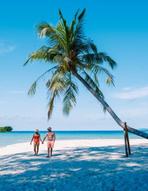 Romantik bir sahne, Tayland 'daki Koh Kood Adası' nın yumuşak, beyaz kumlarında el ele yürürken başlar. Canlı mavi gökyüzü ve nazik dalgalar mükemmel bir tropikal atmosfer yaratır..