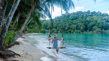 Kumda yalın ayak, Koh Kood Adası 'nın turkuaz sularında sallanan tek bir figür. Bereketli palmiye ağaçları sakin sahneyi çevreleyerek mükemmel bir tropikal kaçış yaratıyor..