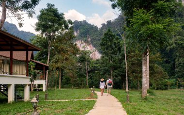 Ziyaretçiler, Tayland 'da lüks bir çevre beldesinde yemyeşil ve yüksek kireçtaşı kayalıklarıyla çevrili Khao Sok Ulusal Parkı' nda manzaralı bir patika boyunca yürüyorlar.