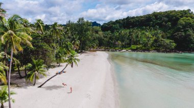 Tayland 'daki Koh Kood Adası' nda yumuşak beyaz kumlar kristal berraklığında sularla buluşur. Bereketli palmiye ağaçları parlak bir gökyüzünün altında hafifçe sallanıyor. Bir çift adam ve bir kadın sahildeki palmiye ağacının altında salıncakta sallanıyorlar.