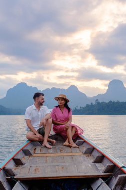 Bir çift, nefes kesen dağlarla çevrili Cheow Lan Gölü 'nde sakin bir tekne yolculuğunun tadını çıkarıyor. Günbatımının altın parıltısı romantik bir atmosfer yaratıyor. Doğada unutulmaz bir deneyim için mükemmel..