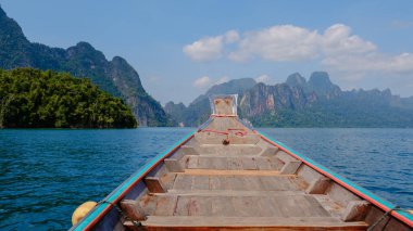 Geleneksel ahşap bir teknenin görkemli kireçtaşı kayalıkları ve yemyeşil Khao Sok, Tayland 'da berrak mavi sularda süzüldüğü yer olan Cheow Lan Gölü' nde sükuneti deneyin.