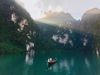 Güneş doğarken Khao Sok, Tayland 'daki Cheow Lan Gölü' nün sakin sularına tanık olun. Uzun kuyruklu bir çift göl boyunca sorunsuzca süzülür. Güneş yükselen uçurumlara altın ışınlar saçar..