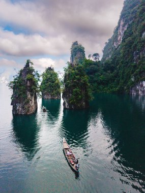 Tayland 'ın Khao Sok kentindeki Cheow Lan Gölü' nün dingin güzelliğini deneyimleyin. Orada, yumuşak bir gökyüzü altında yemyeşil bir yeşil ile çevrili yüksek kireçtaşı kayalıkların arasından geleneksel bir uzun kuyruklu tekne süzülür..