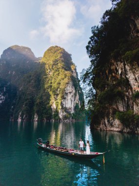 Khao Sok, Tayland 'daki Cheow Lan Gölü' nde nefes kesici bir an. Güneşli bir günde sakin sulara yansıyan büyüleyici kireçtaşı kayalıkları olan geleneksel bir teknede bir çifti sergiliyorlar..