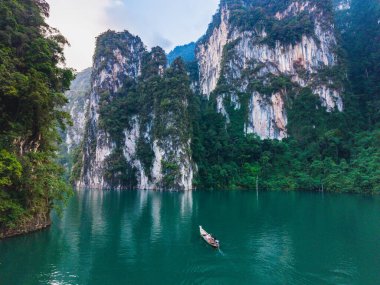 Zümrüt sularının yemyeşil çimenliklerle çevrili yüksek kireçtaşı kayalıkları yansıttığı büyüleyici Cheow Lan Gölü manzarasını keşfedin. Khao Sok Tayland