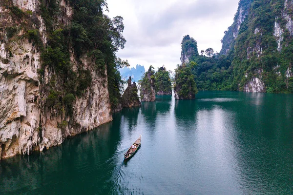 Khao Sok, Tayland 'daki Cheow Lan Gölü' nün sakin sularını deneyin. Uzun bir tekne zümrüt sularda süzülüyor, görkemli kireçtaşı kayalıkları ve yemyeşil kayalıklarla çerçevelenmiş, huzurlu bir geri çekilme yaratıyor..