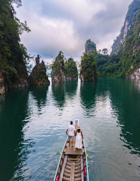 Yeşillik ve yüksek kireçtaşı kayalıklarıyla çevrili Cheow Lan Gölü 'nün sakin atmosferini hissedin. Khao Sok Tayland 'da uzun kuyruklu bir teknenin önünde bir çift.