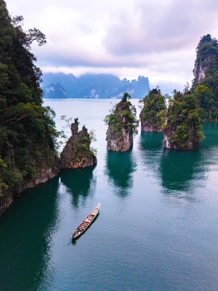 Cheow Lan Gölü 'nün sakin suları şafakta karst oluşumlarını yansıtır. Geleneksel bir tekne, yemyeşil ve sisli dağ zirveleri olan Khao Sok Tayland 'da huzur içinde süzülür.