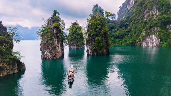 Cheow Lan Gölü 'nün sakin manzarası, yemyeşil ağaçlarla çevrili yüksek kireçtaşı kayalıkları sergiliyor. Geleneksel bir tekne zümrüt sularında usulca süzülür, doğanın güzelliğini gösterir..
