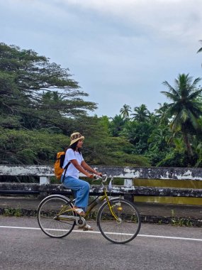Tayland 'da Khao Sok' un güzel manzaralarını keşfeden bir bisikletçi, huzurlu bir yol boyunca güvenle ilerliyor. Yükselen ağaçlar ve canlı yapraklar açık hava maceraları için cennet bir zemin oluşturur..