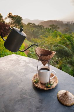 Tayland 'da, Khao Sok' ta, sisli tepelerin canlı yeşillikle buluştuğu yerde damlalar halinde kahve yapmak. Sıcak bir bardağın tadını çıkarırken huzurun tadını çıkarmak için mükemmel bir an..