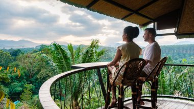 Bir çift büyüleyici bir balkonda oturuyor, Tayland 'daki Khao Sok Ulusal Parkı' nın verimli manzaralarının üzerinde nefes kesen güneşin altında.