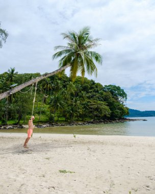 Koh Kood Adası 'nda sakin bir an. Kıyıdaki palmiye ağacından nazikçe sarkan bir adam gibi. Yumuşak kum ve yemyeşil yeşil Tayland 'da bulutlu bir gökyüzünün altında mükemmel bir tropikal kaçış yaratır.