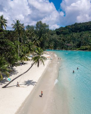 Ziyaretçiler, Tayland 'ın Koh Kood Adası' nda güneşli bir plajın keyfini çıkarıyorlar. Bereketli palmiye ağaçları kıyı şeridini çevrelerken, turkuaz sular yüzme ve rahatlamaya davetiye çıkarıyor..