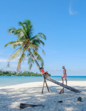 İki arkadaş, Tayland 'daki Koh Kood Adası' nda güneşli bir günün tadını çıkarıyorlar. Palmiye ağacında sallanıyorlar ve yumuşak beyaz kumlarda birlikte gülüyorlar. Turkuaz okyanus tropikal cennet atmosferine katılır..