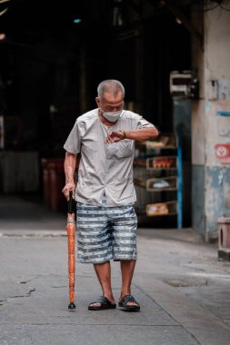 Bangkok, Tayland, 19 Kasım 2025, Talat Phlu 'nun dar bir sokağında elinde şemsiyeyle nöbet tutan yaşlı bir adam duruyor. Hareketli atmosfer yerel yaşamı ve kültürü yakalıyor..