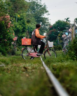 Bangkok, Tayland, 19 Kasım 2025 Talat Phlu 'da bir bisikletçi, çevresi yeşillik ve yerel yaşamla çevrili sakin bir ara sokakta geziniyor ve şehirdeki bu gizli mücevherin cazibesini sergiliyor..