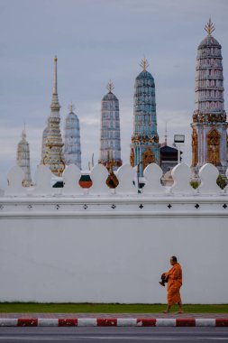 Bangkok, Tayland, 19 Kasım 2025, Wat Phra Kaew 'ın yanında huzur içinde yürüyen sakin bir keşiş sahnesi, akşam gökyüzünün altında renkli kuleleri sergiliyor..