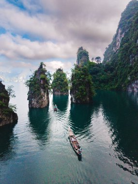 Khao Sok, Tayland 'daki Cheow Lan Gölü' nün dingin güzelliğini keşfedin. Uzun kuyruklu bir teknede güneşin doğuşunu izleyen bir çift.