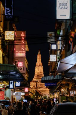 Bangkok, Tayland, 19 Kasım 2025 Wat Arun, Şafak Tapınağı 'nı çevreleyen hareketli sokak yaşamı, yerel halk ve turistler yakınlardaki dükkanları ve lokantaları keşfederken gece gökyüzünü aydınlatıyor..