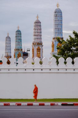 Bangkok, Tayland, 19 Kasım 2025. Bir keşiş, Wat Phra Kaew 'in ikonik tapınaklarının yanından geçerken gün doğumunun yumuşak parıltısıyla yıkanırken huzurlu bir manzara beliriyor..