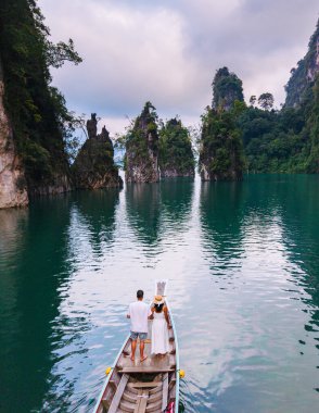İki gezgin, Tayland 'ın Khao Sok kentindeki Cheow Lan Gölü' nde çarpıcı kireçtaşı kayalıkları ve zümrüt sularıyla çevrili geleneksel bir teknede duruyorlar. Huzurlu atmosfer macerayı davet eder..