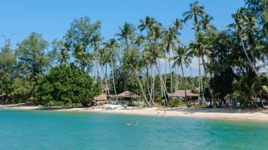 Ziyaretçiler Koh Kood Adası 'nın sakin sahillerinde güneşli bir günün tadını çıkarıyorlar. İnsanlar yüzdükçe sallanan gür palmiye ağaçları, Ao Taphao Sahili