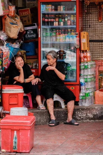 Bangkok, Tayland, 19 Kasım 2025, Çin Mahallesi 'nde renkli ürünlerle dolu bir dükkânın önünde iki kadının gülüp sohbet ettiği canlı bir sahne..