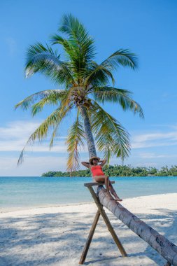 Bir kadın, Koh Kood Adası 'nın güzel sahillerinde güneşli bir günün tadını çıkarır. Bir palmiye ağacına yaslanır, berrak mavi gökyüzü ve yumuşak kumla sakin atmosferde güneşlenir..