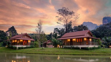 Tayland 'da, Khao Sok' ta sakin bir göl yakınında yeşilliklerle çevrili rahat pansiyonlar. Parlak günbatımı gökyüzüne huzur ve güzellik arayan gezginler için mükemmel sakin bir atmosfer ekler..