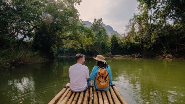 İki maceracı, yemyeşil ve çarpıcı kaya oluşumlarıyla çevrili Tayland, Khao Sok 'ta bir bambu salında huzur içinde yüzerler..