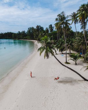 Yumuşak kum ve sallanan palmiye ağaçlarıyla Koh Kood Adası 'nda sakin bir günün tadını çıkar. Ziyaretçiler rahatlar ve Tayland 'ın saklı cennetinin berrak sularıyla çevrili bir palmiye ağacının altında salıncakta sallanırlar.