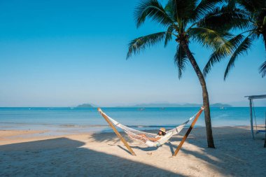 Tayland 'daki Koh Phayam Adası' nın sakin sahillerinde bir hamakta uzanırken güneşi emmek. Açık mavi gökyüzü ve nazik dalgalar mükemmel bir tropikal kaçış yaratır..
